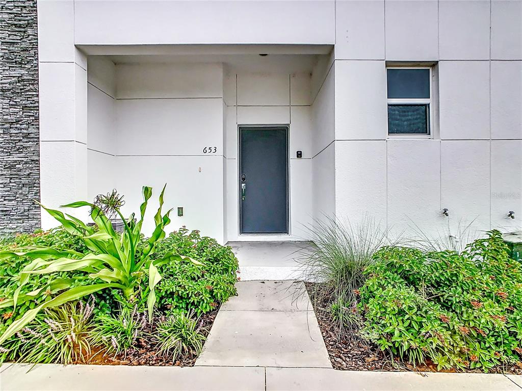 A modern home entrance features a dark door, white panel siding, and landscaped garden beds — 653 TRIKOMO DRIVE, DAVENPORT, FL