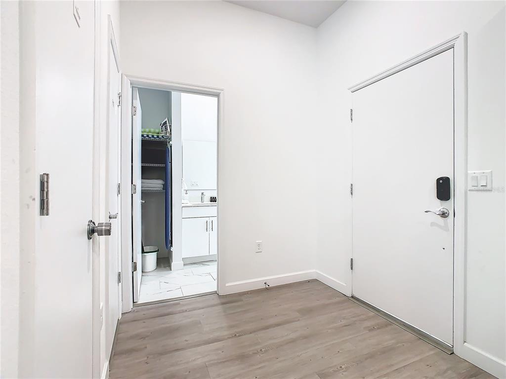 An entryway with wood-look flooring leads to a doorway revealing a bathroom with white cabinets — 653 TRIKOMO DRIVE, DAVENPORT, FL