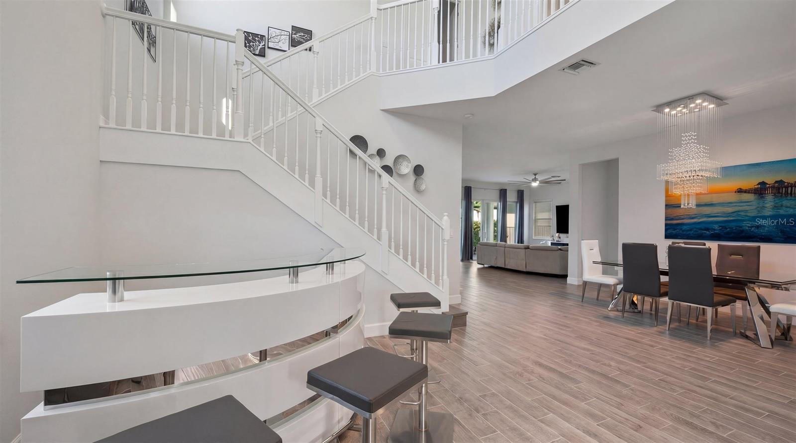 A modern foyer features a curved white bar, a staircase, and a dining area beyond — 4619 Citron Way, Westlake FL 33470, WESTLAKE, FL