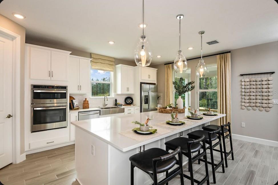 A modern kitchen features white cabinets, a large quartz island, and three glass pendant lights — 8 ARMENIA COURT, PALM COAST, FL