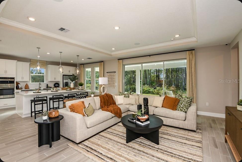 A bright open-concept living room features a large sectional sofa, kitchen island, and sliding glass doors — 8 ARMENIA COURT, PALM COAST, FL