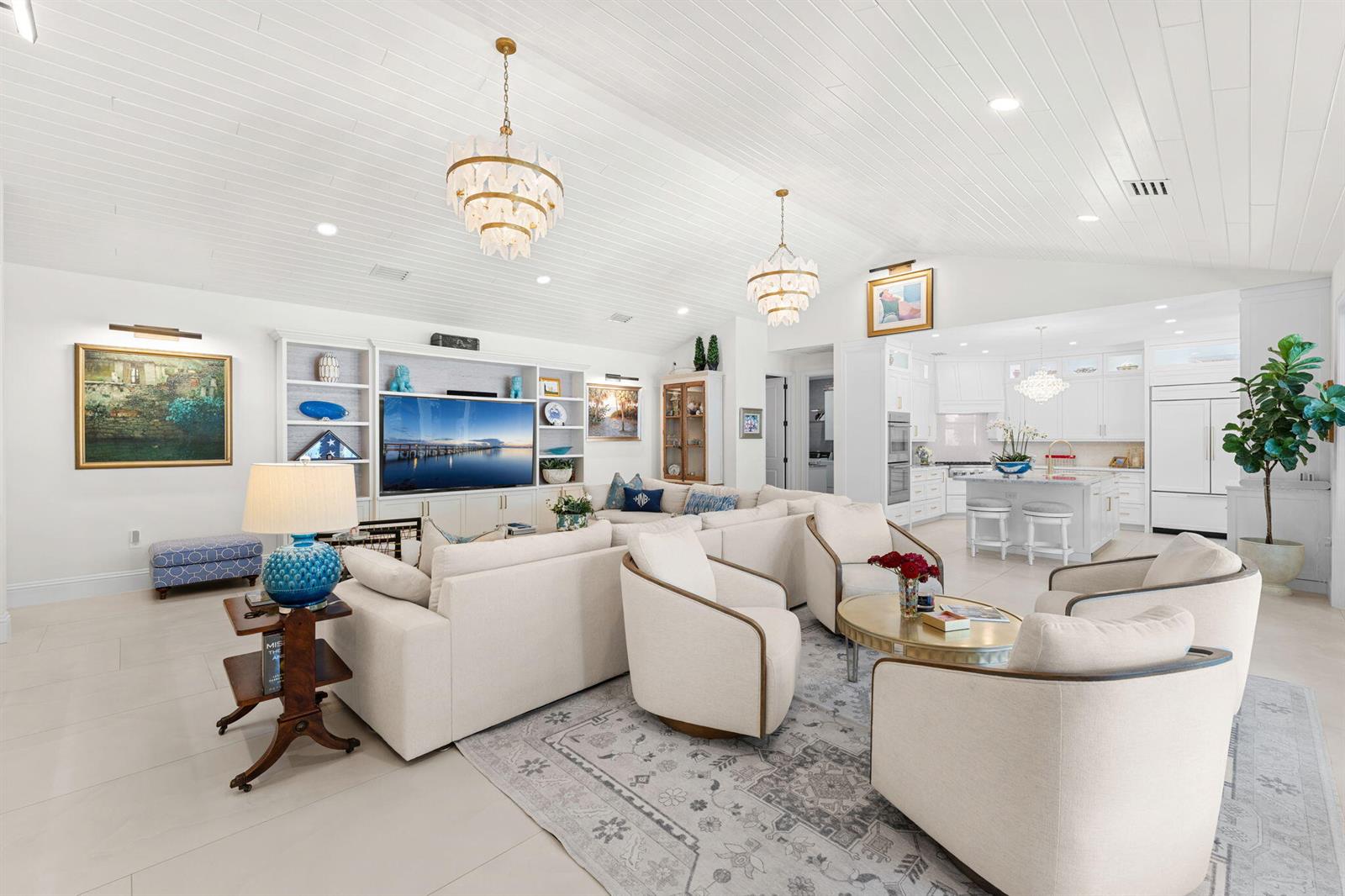 A bright, open-concept living room and kitchen featuring white cabinetry, vaulted ceilings, and chandeliers — 906 Jasmine Lane, Vero Beach FL 32963, VERO BEACH, FL