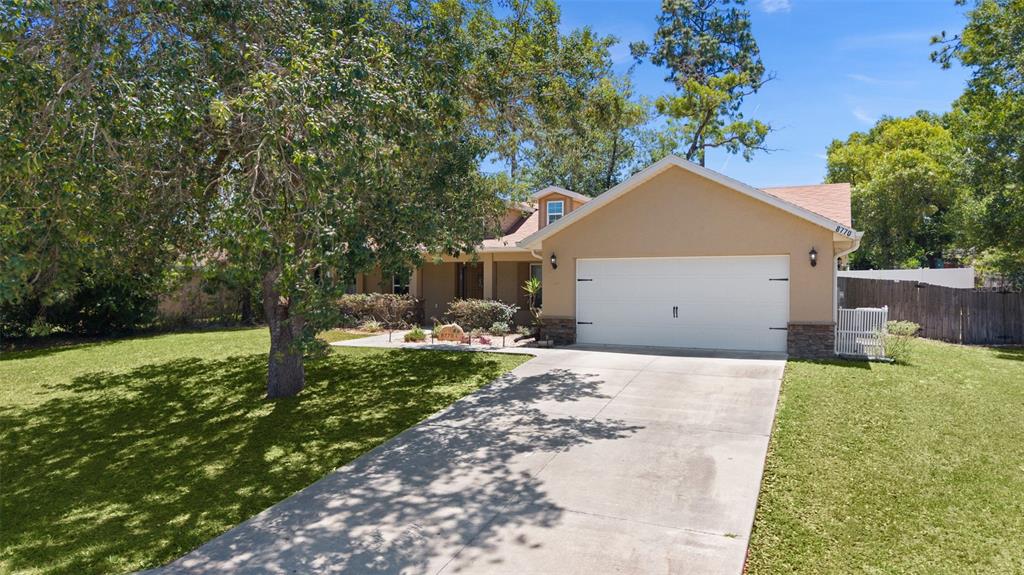 A tan house with a white garage door and a concrete driveway sits on grass — 8770 SE 161ST STREET, SUMMERFIELD, FL
