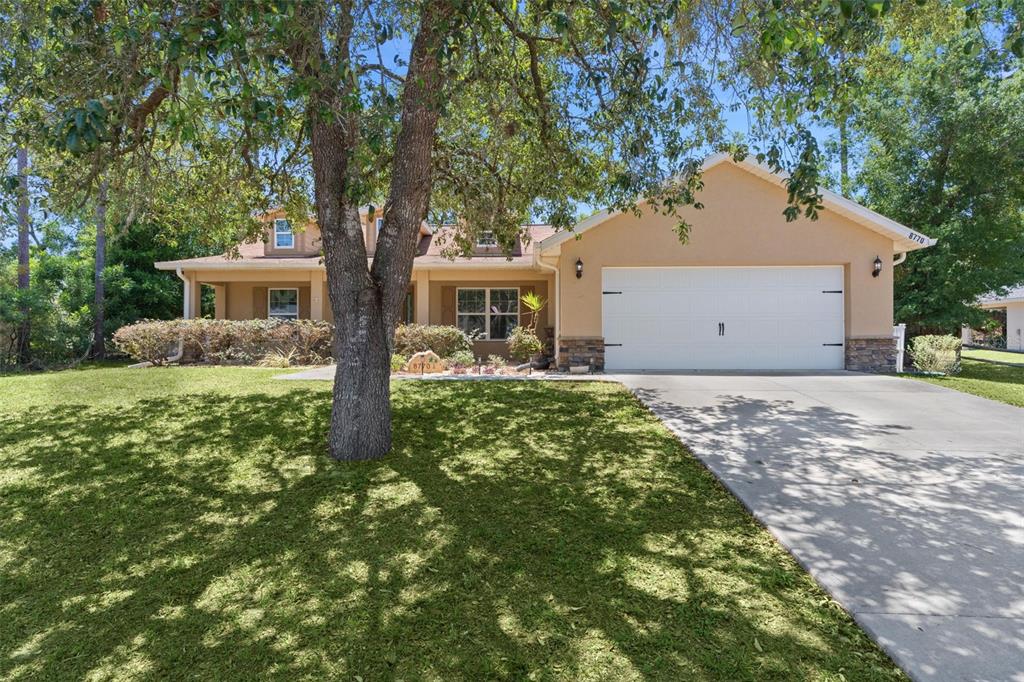 A single-story house with a beige stucco exterior, a two-car garage, and a large tree — 8770 SE 161ST STREET, SUMMERFIELD, FL