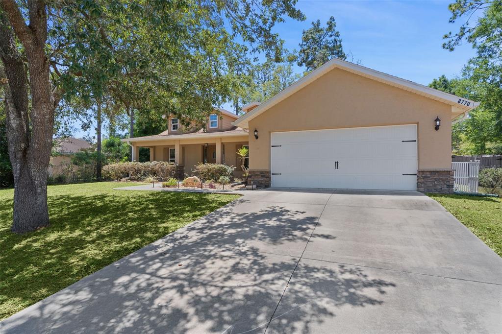 A tan house with a white garage door and a front porch sits behind a driveway — 8770 SE 161ST STREET, SUMMERFIELD, FL