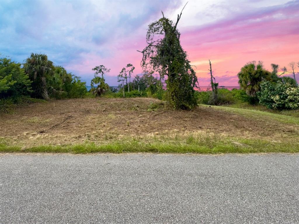 A vacant, cleared lot with trees and shrubs overlooks the water at sunset — LOT 28 FLORALA STREET, NORTH PORT, FL