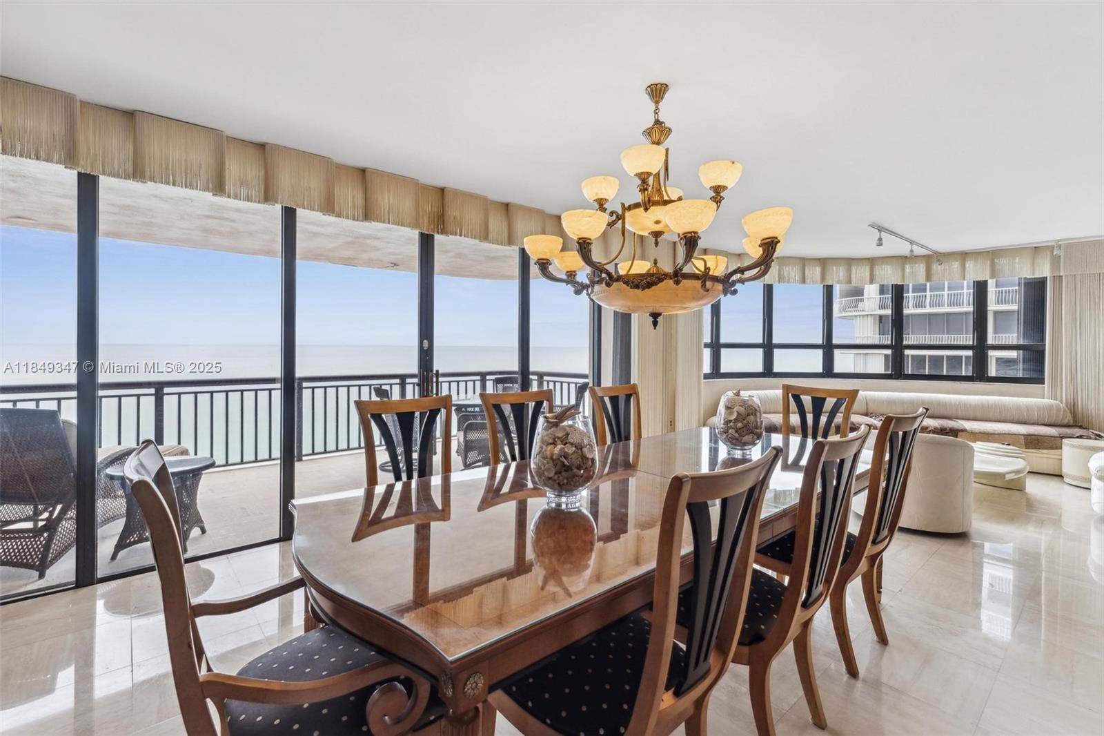 A dining room features a glass-topped table, ornate chandelier, and floor-to-ceiling windows overlooking the ocean — 10175 Collins Ave # 1202, Bal Harbour FL 33154, BAL HARBOUR, FL