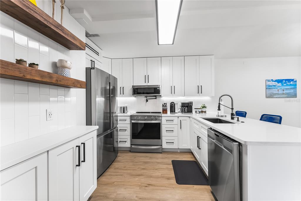 A modern kitchen features white cabinetry, stainless steel appliances, wood shelving, and a white island — 4501 S ATLANTIC AVENUE UNIT 213, NEW SMYRNA BEACH, FL