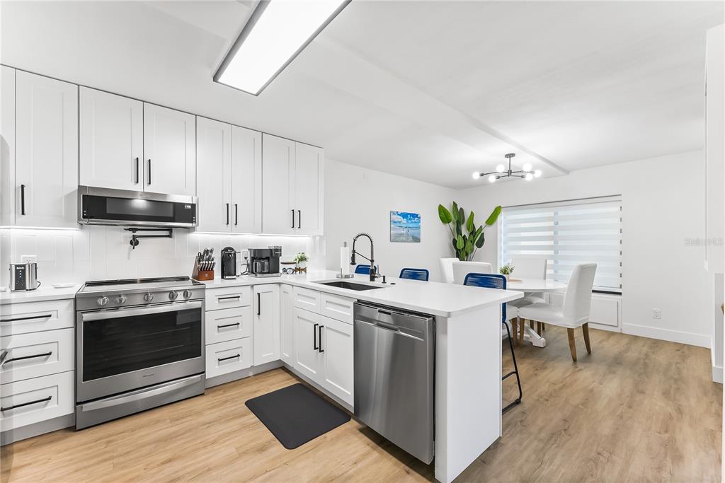 A modern kitchen features white cabinets, stainless steel appliances, and a dining area with seating — 4501 S ATLANTIC AVENUE UNIT 213, NEW SMYRNA BEACH, FL