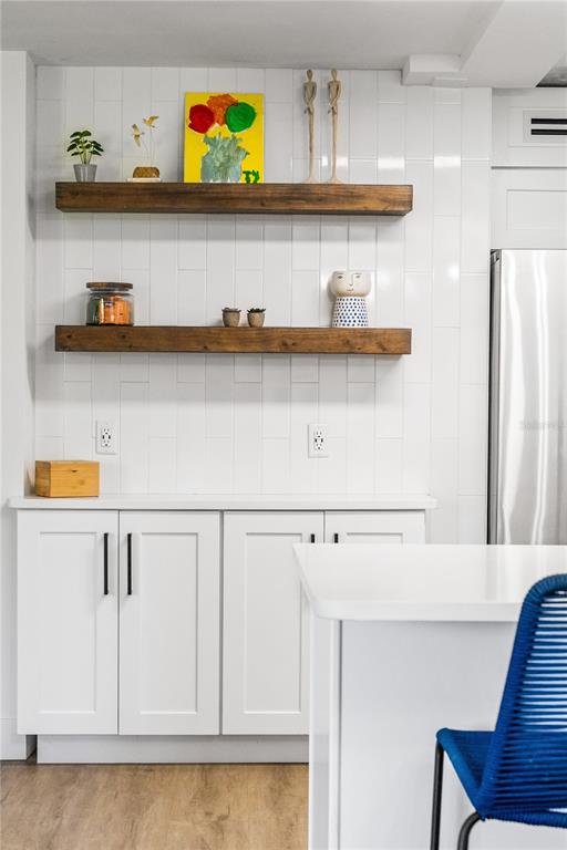 A kitchen features white cabinets, two wooden floating shelves, and a white tiled backsplash — 4501 S ATLANTIC AVENUE UNIT 213, NEW SMYRNA BEACH, FL