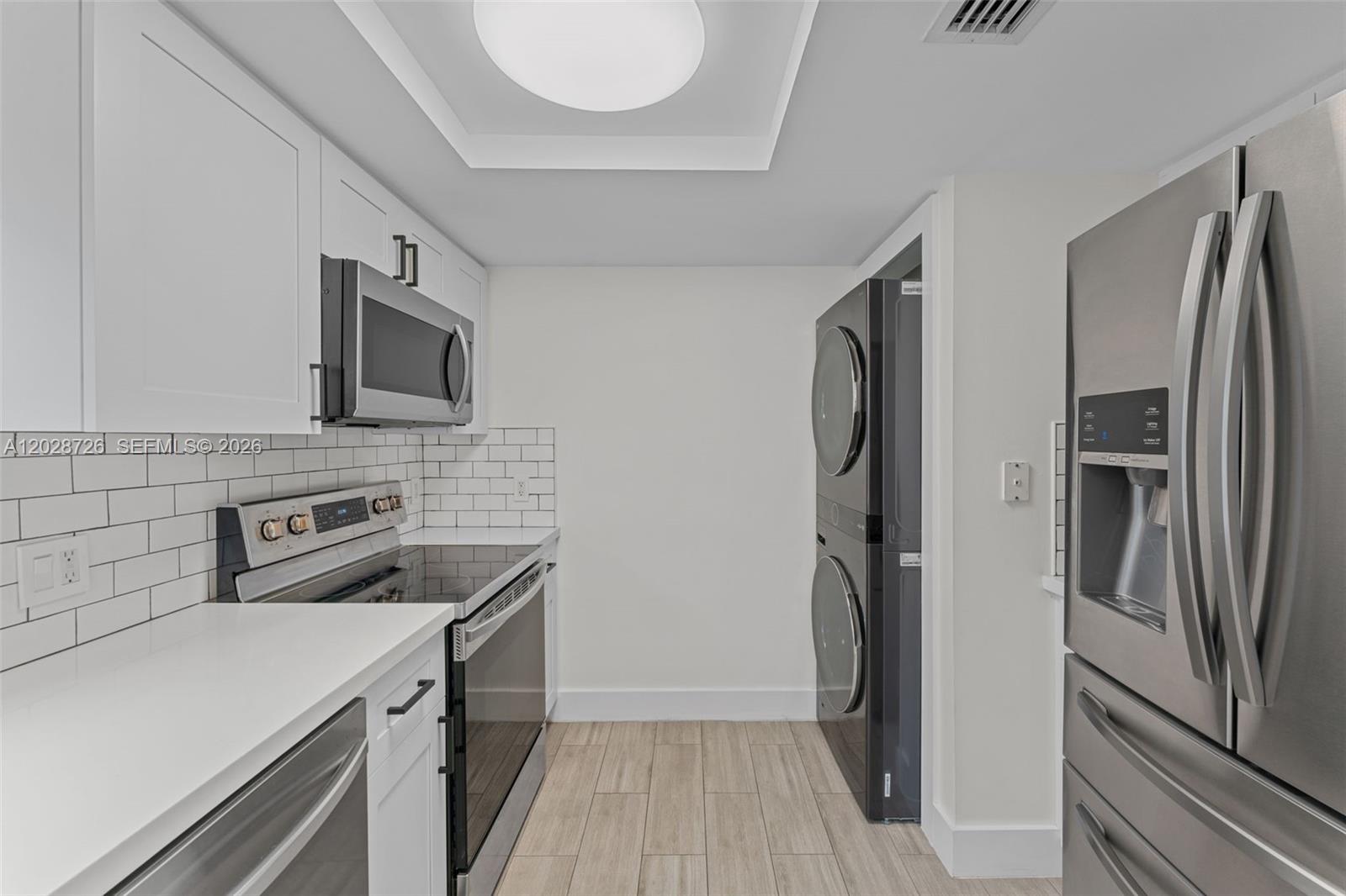 A kitchen features white cabinets, stainless steel appliances, a subway tile backsplash, and stacked laundry — 2415 NW 16th St Rd # 306, Miami FL 33125, MIAMI, FL