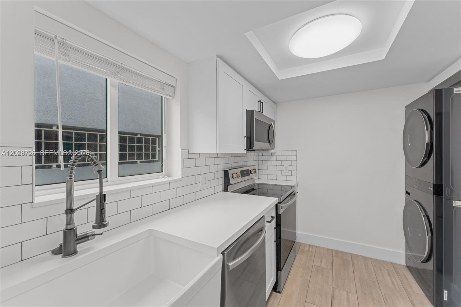 A modern kitchen features white cabinets, subway tile backsplash, stainless steel appliances, and stacked laundry — 2415 NW 16th St Rd # 306, Miami FL 33125, MIAMI, FL