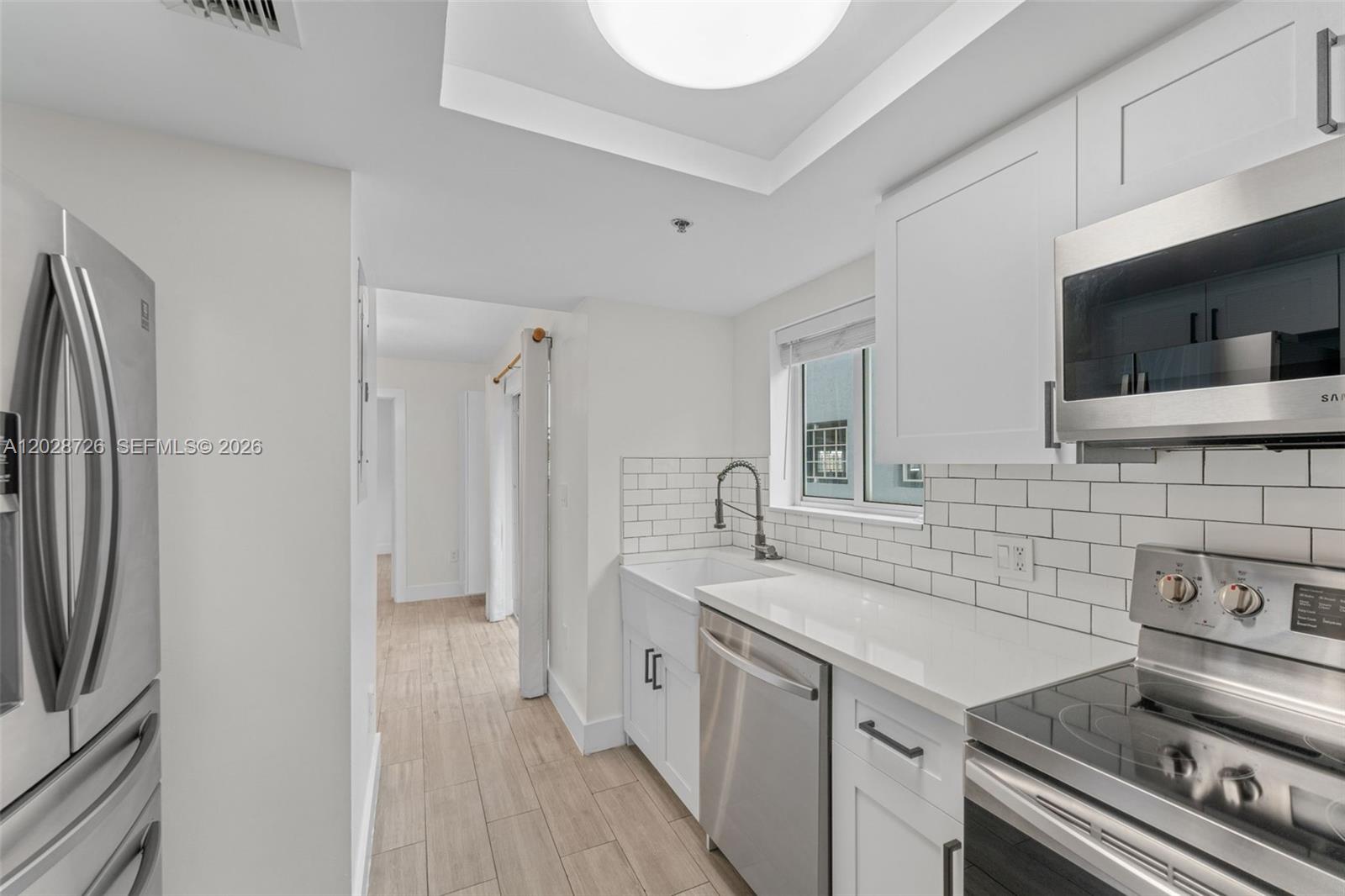 A modern kitchen features white cabinets, subway tile backsplash, stainless steel appliances, and wood-look flooring — 2415 NW 16th St Rd # 306, Miami FL 33125, MIAMI, FL