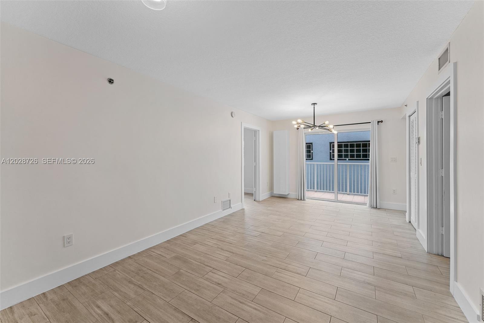 This empty living room features light wood-look tile flooring, a modern chandelier, and a balcony — 2415 NW 16th St Rd # 306, Miami FL 33125, MIAMI, FL