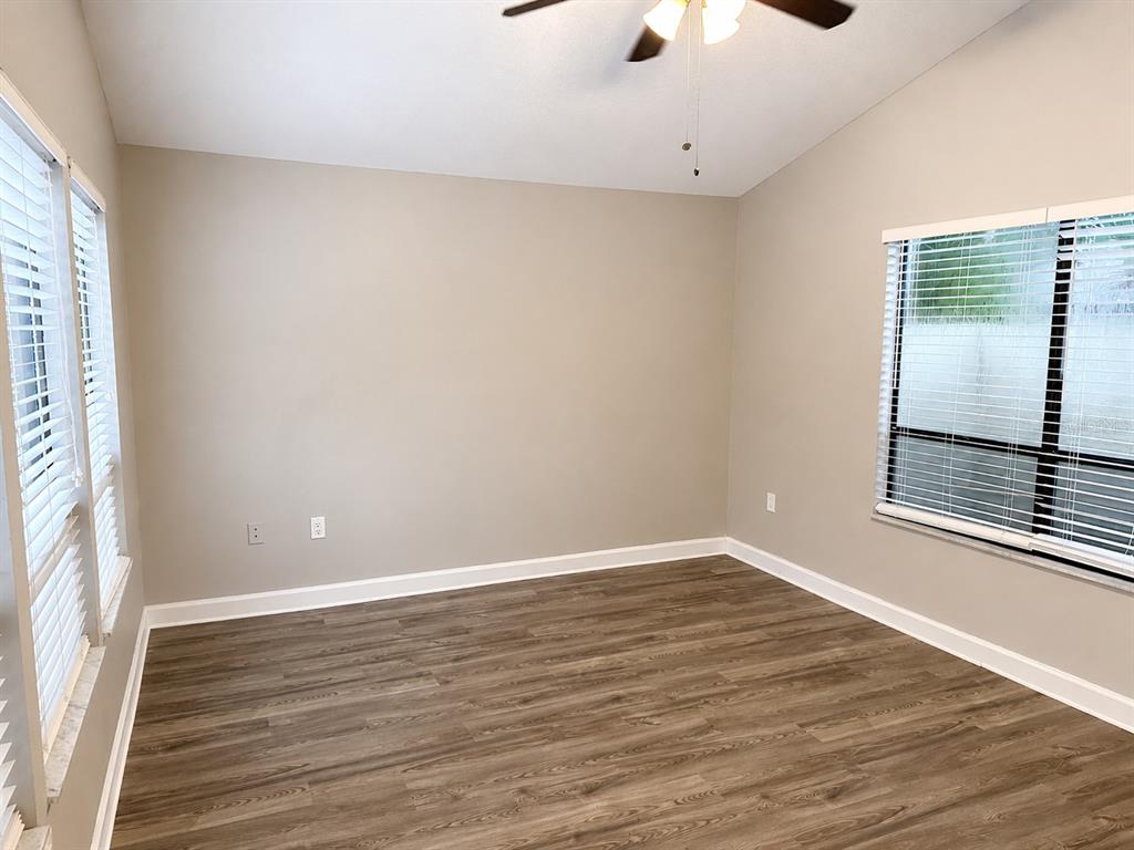 An empty room features light gray walls, wood-look flooring, a ceiling fan, and large windows — 664 CHANNING DRIVE, PALM HARBOR, FL