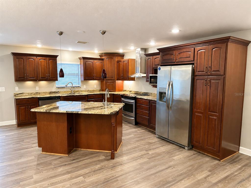 A kitchen features dark wood cabinetry, granite countertops, a center island, and stainless steel appliances — 664 CHANNING DRIVE, PALM HARBOR, FL