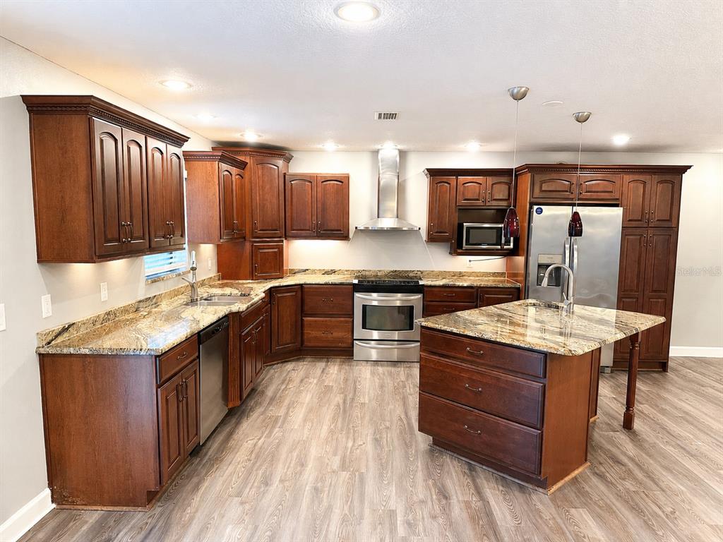 A kitchen features dark wood cabinets, granite countertops, stainless steel appliances, and a center island — 664 CHANNING DRIVE, PALM HARBOR, FL