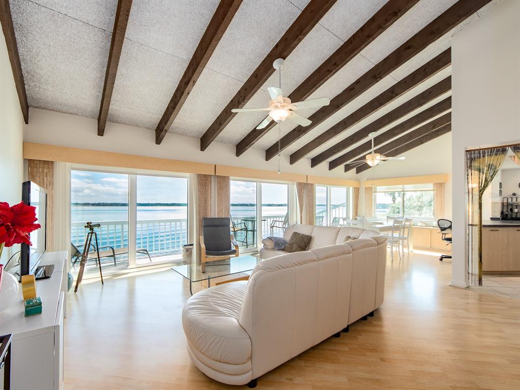 A living room with vaulted beamed ceilings, white leather sofa, and large windows overlooking water — 1401 GULF BOULEVARD UNIT 215, CLEARWATER BEACH, FL
