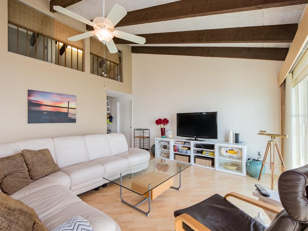 A living room features a white sectional sofa, glass coffee table, and exposed ceiling beams — 1401 GULF BOULEVARD UNIT 215, CLEARWATER BEACH, FL