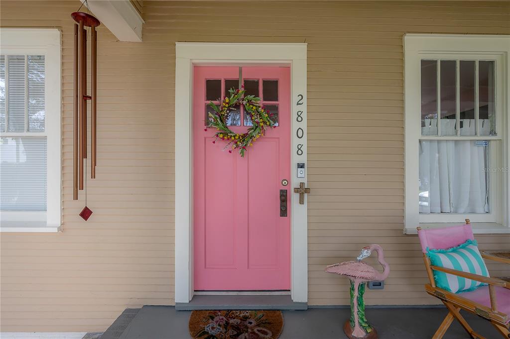A pink front door with a floral wreath is centered on a tan porch — 2808 W AQUILLA STREET, TAMPA, FL