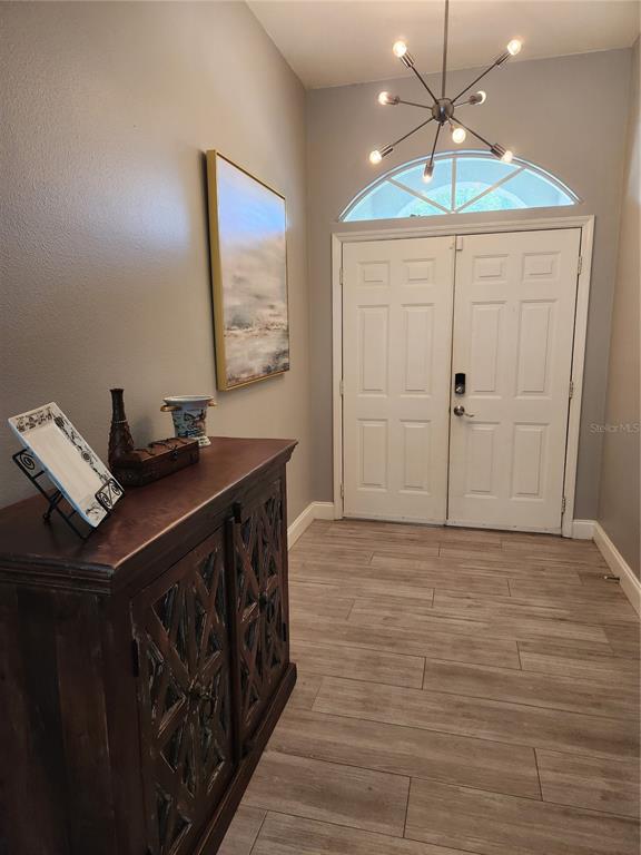 An entryway features a dark wood cabinet, a modern chandelier, and light wood-look tile flooring — 5274 FAR OAK CIRCLE, SARASOTA, FL