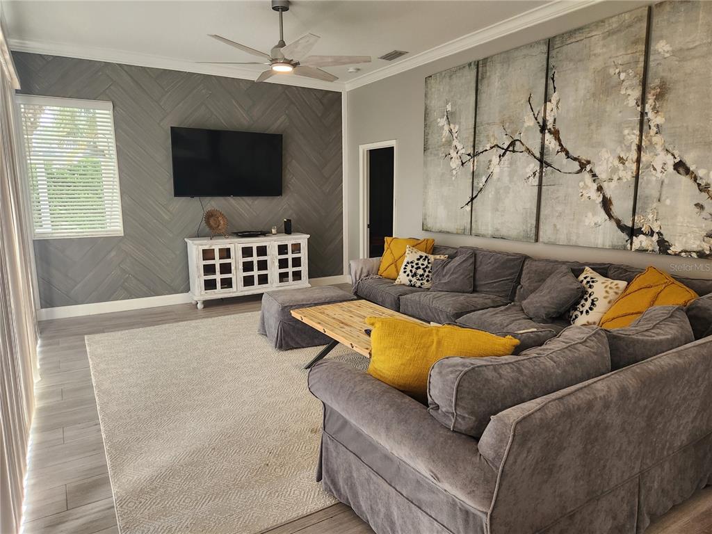 A living room features a grey herringbone accent wall, sectional sofa, and large floral artwork — 5274 FAR OAK CIRCLE, SARASOTA, FL