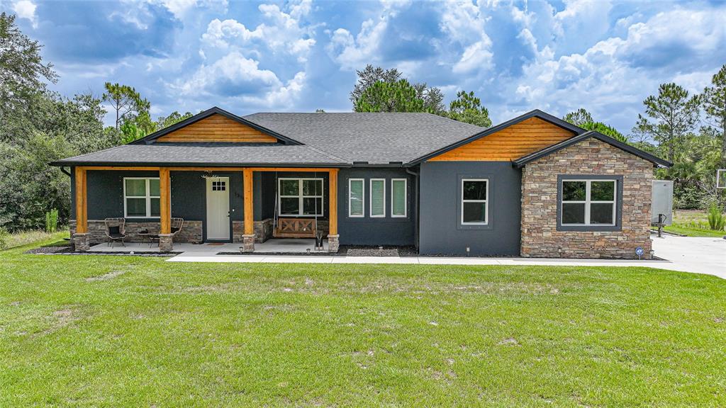 A single-story house features dark gray siding, stone accents, wood trim, and a covered porch — 13190 BANYAN DRIVE, PUNTA GORDA, FL