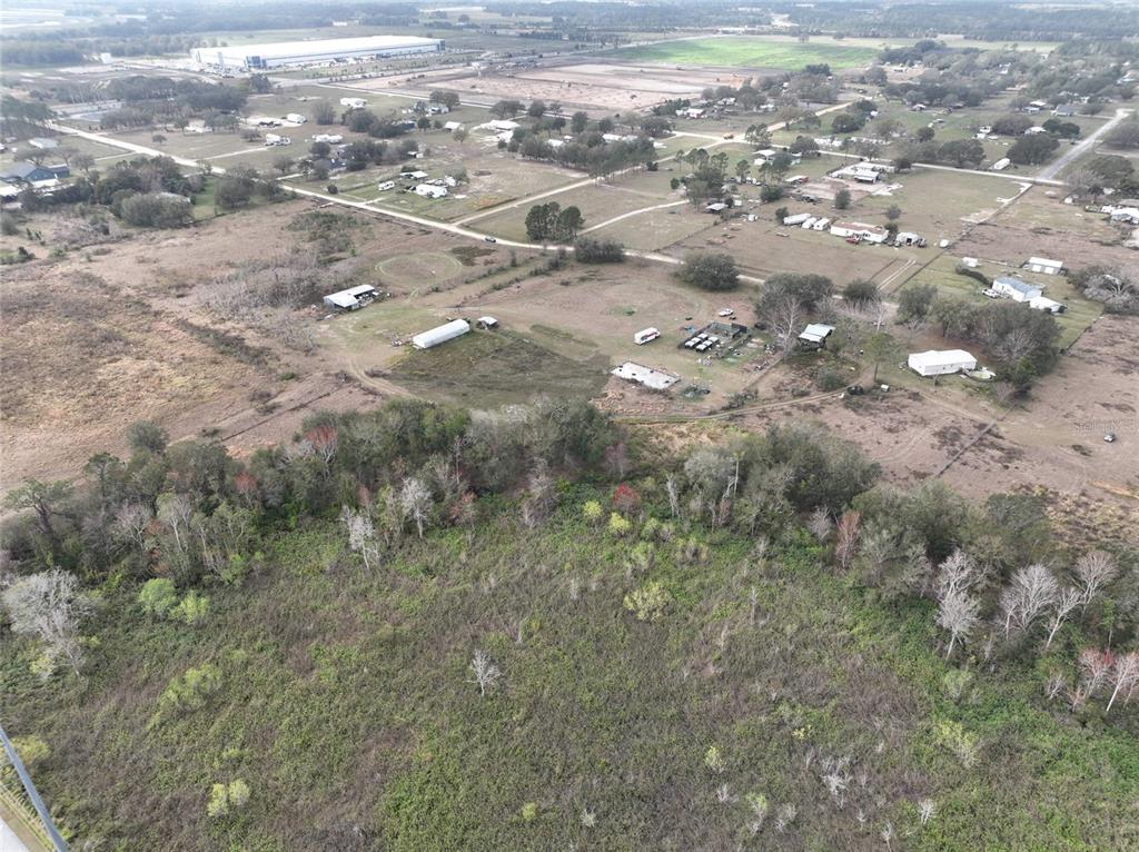 An aerial view shows a large, undeveloped grassy lot bordered by trees and nearby houses — 307 & 317 SKYBLUE LANE, AUBURNDALE, FL