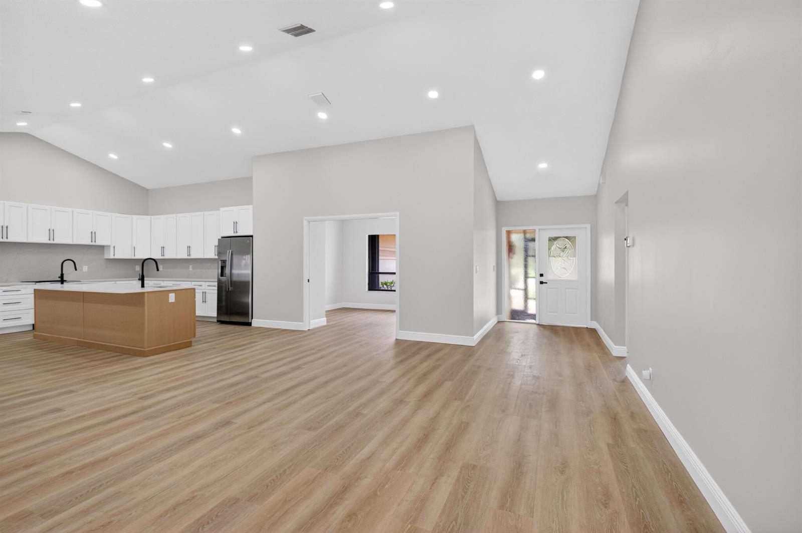 An open-concept kitchen and living area features light wood flooring, white cabinetry, and recessed lighting — 9362 Laurel Green Drive, Boynton Beach FL 33437, BOYNTON BEACH, FL