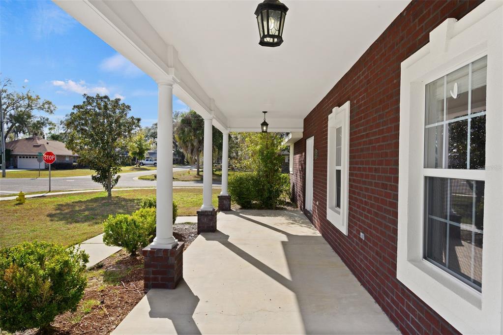 A covered brick porch features white columns and a concrete floor overlooking a suburban street — 25178 SW 20TH AVENUE, NEWBERRY, FL