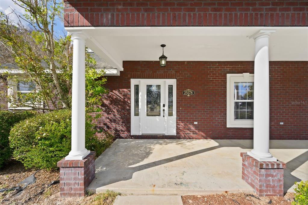 A brick house exterior features a covered front porch with two white columns and a door — 25178 SW 20TH AVENUE, NEWBERRY, FL