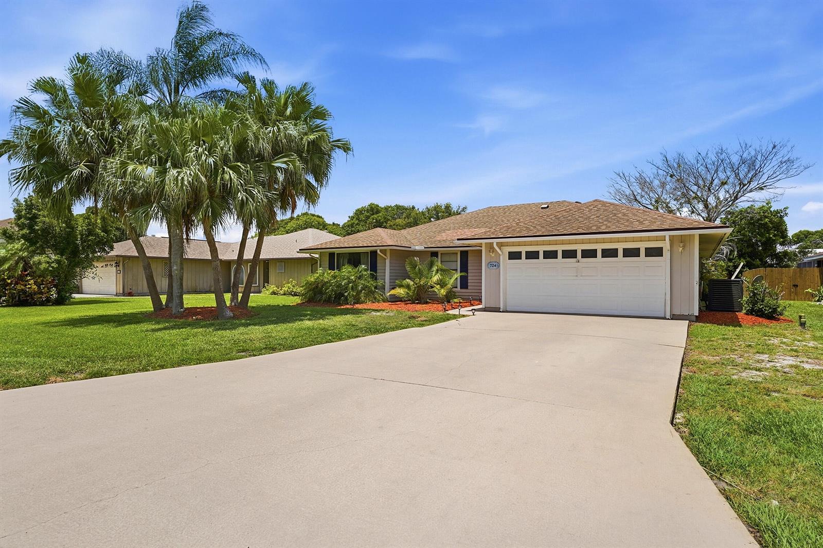 A single-story house with a white garage door, tan siding, and palm trees in front — 724 24th Square, Vero Beach FL 32962, VERO BEACH, FL