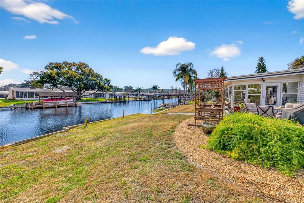 A grassy backyard overlooks a canal with boat docks and neighboring homes under a sky — 1018 SOUTHLAND DRIVE, TAVARES, FL