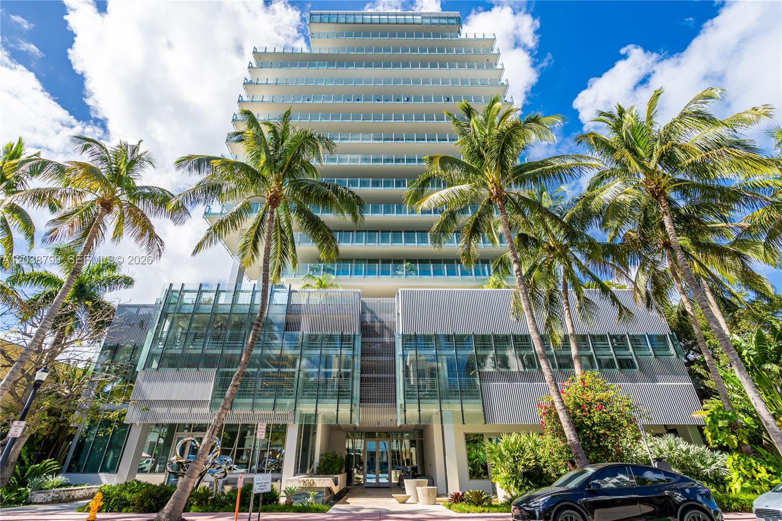 A modern high-rise building with glass balconies stands behind palm trees and a black car — 120 Ocean Dr # 700, Miami Beach FL 33139, MIAMI BEACH, FL
