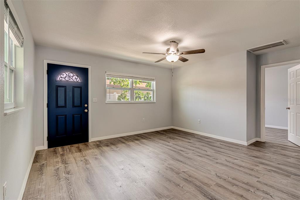 An empty room features light gray walls, wood-look flooring, a ceiling fan, and a blue door — 7391 34TH STREET N, PINELLAS PARK, FL