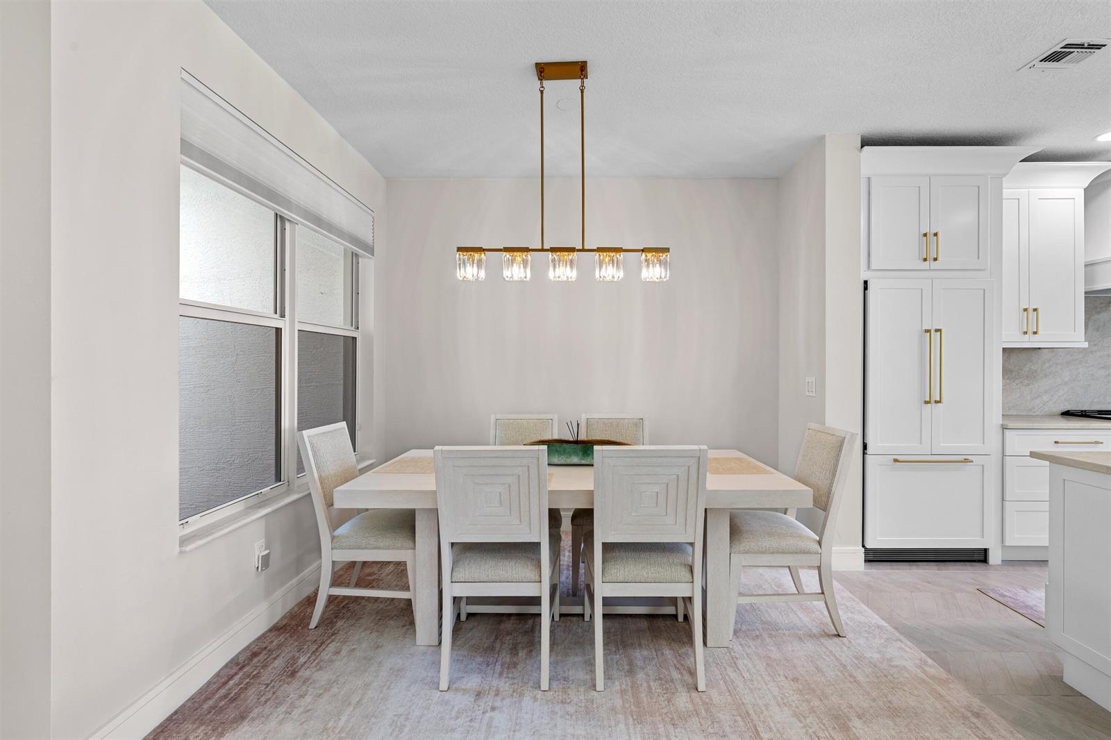 A dining room features a rectangular table, six chairs, and a modern gold linear chandelier — 1570 NW 48th Place, Boca Raton FL 33431, BOCA RATON, FL