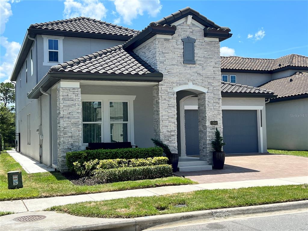 A two-story house features a stone facade, gray stucco walls, and a dark tile roof — 12640 SALOMON COVE DRIVE, WINDERMERE, FL