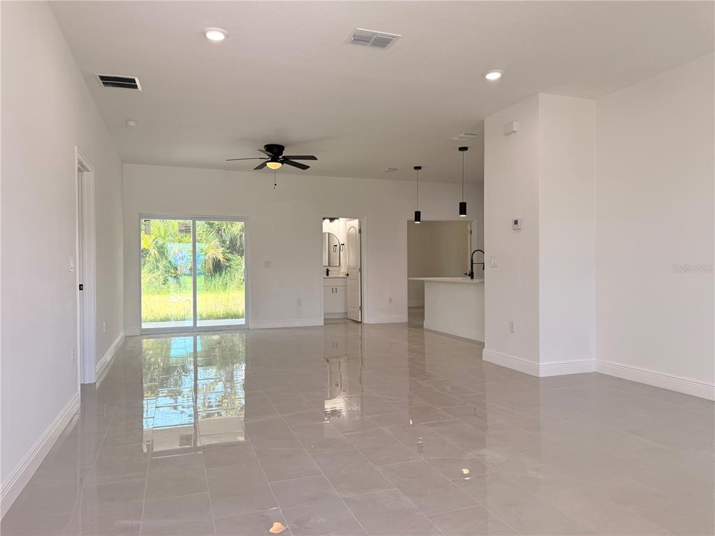 An open-concept living area features light-colored tile flooring, a ceiling fan, and sliding glass doors — 1251 SCOTTISH STREET SW, PALM BAY, FL