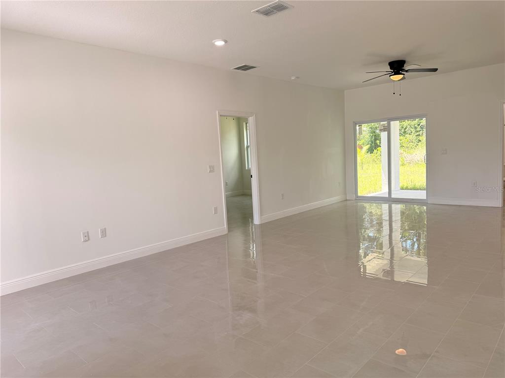 A spacious, empty living room features light-colored tile flooring, white walls, and sliding glass doors — 1251 SCOTTISH STREET SW, PALM BAY, FL