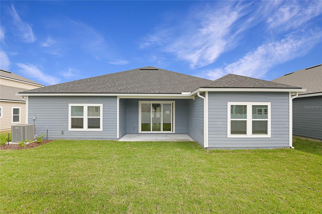 The rear exterior of a single-story blue house features a patio and a grassy yard — 34 WINDMILL PALM WAY, PALM COAST, FL
