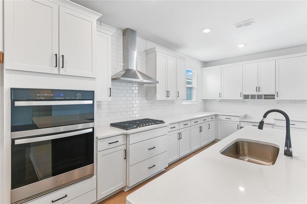 A modern kitchen features white cabinetry, a large island, stainless steel appliances, and subway tile — 34 WINDMILL PALM WAY, PALM COAST, FL