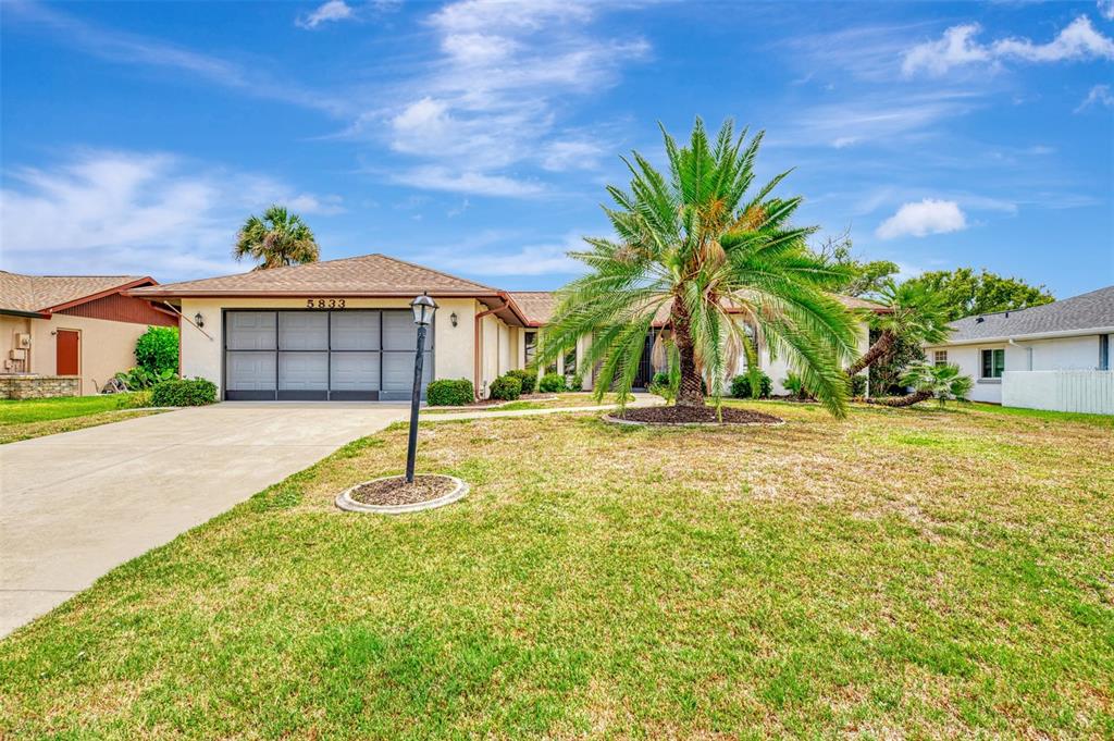 A single-story house with a two-car garage, a large palm tree, and a grassy lawn — 5833 MADISON ROAD, VENICE, FL