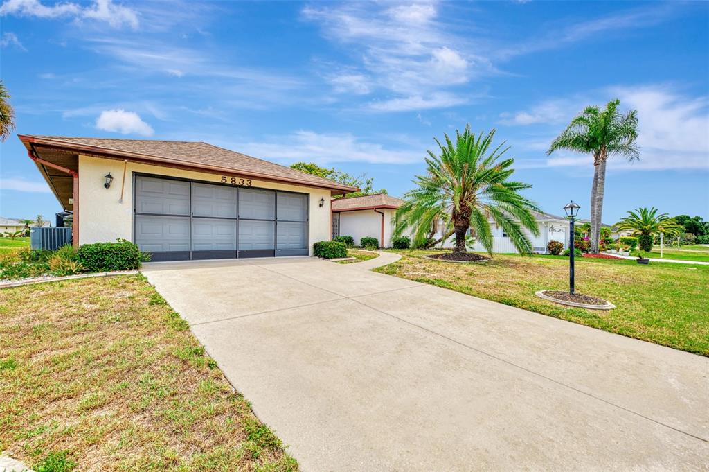 A single-story house with a concrete driveway, a garage with a screen door, and palm trees — 5833 MADISON ROAD, VENICE, FL