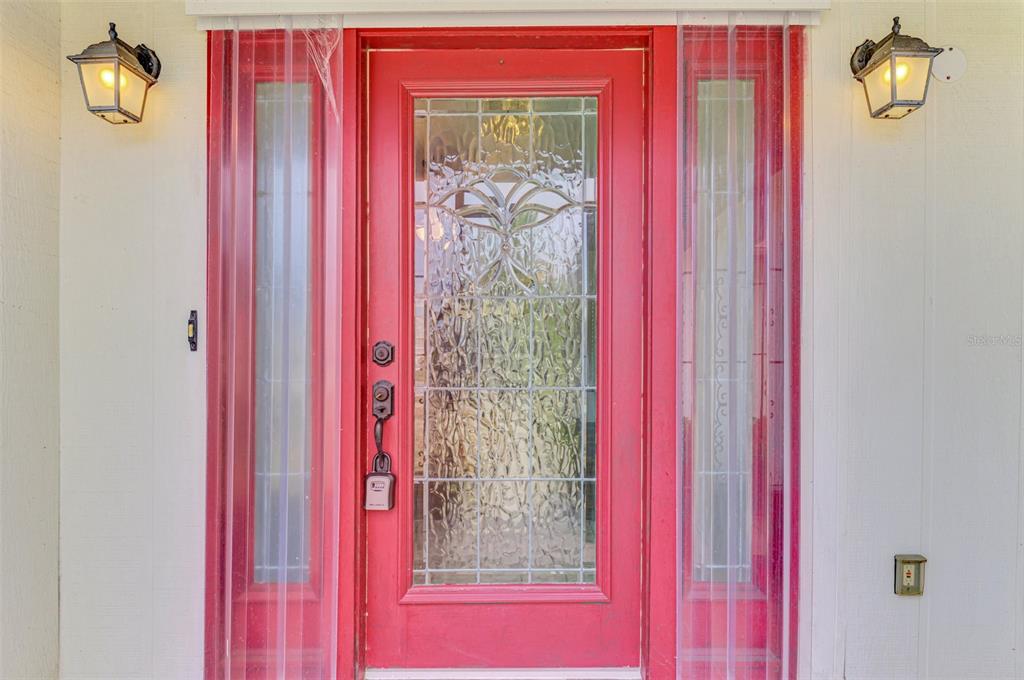 A red front door with a decorative glass insert and sidelights is flanked by two lanterns — 5833 MADISON ROAD, VENICE, FL