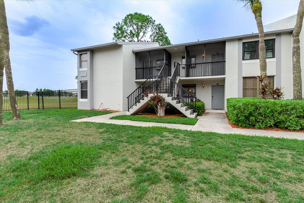 An exterior view of a two-story apartment building with a central staircase and screened balconies — 2073 SKIMMER COURT W UNIT 222, CLEARWATER, FL