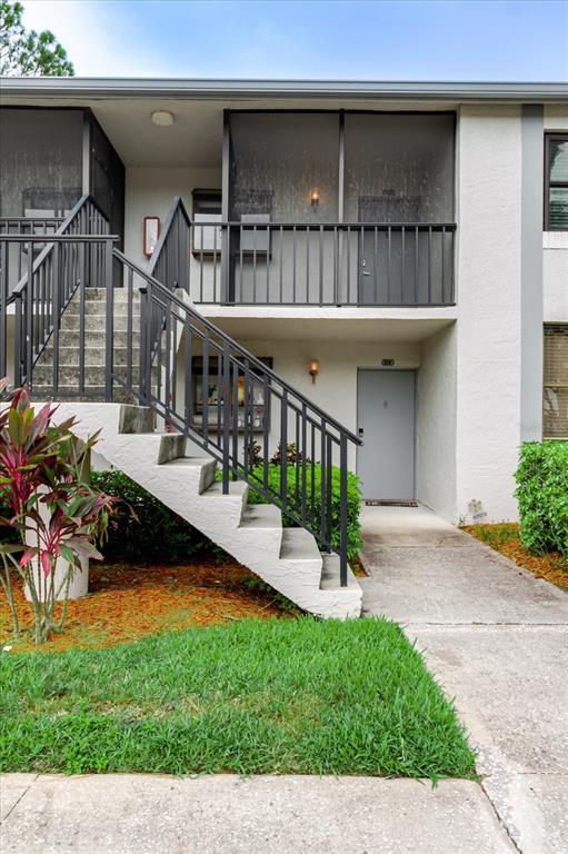 An exterior view shows a two-story apartment building with a concrete staircase and screened balcony — 2073 SKIMMER COURT W UNIT 222, CLEARWATER, FL