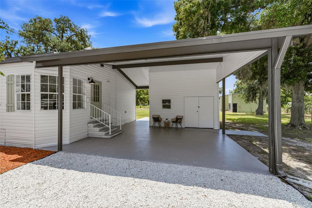 A white house features a large covered carport with a concrete floor and outdoor seating — 5005 SUGAR OAK LANE, DOVER, FL