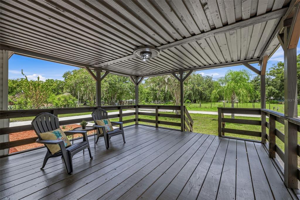 A covered wooden deck features two chairs and overlooks a grassy yard with trees — 5005 SUGAR OAK LANE, DOVER, FL
