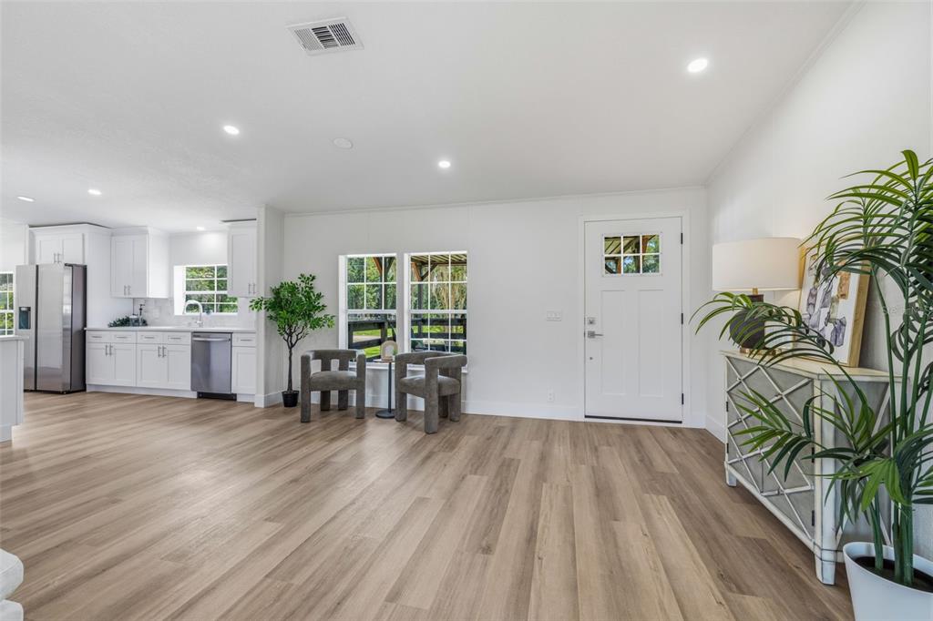 A bright, open-concept living area features light wood-look flooring, white walls, and an adjacent kitchen — 5005 SUGAR OAK LANE, DOVER, FL