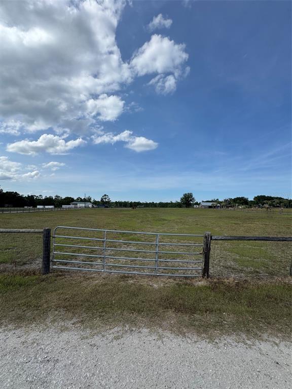 A metal gate opens into a large, grassy fenced pasture under a blue sky — 807 CAMPBELL LANE, DE LEON SPRINGS, FL